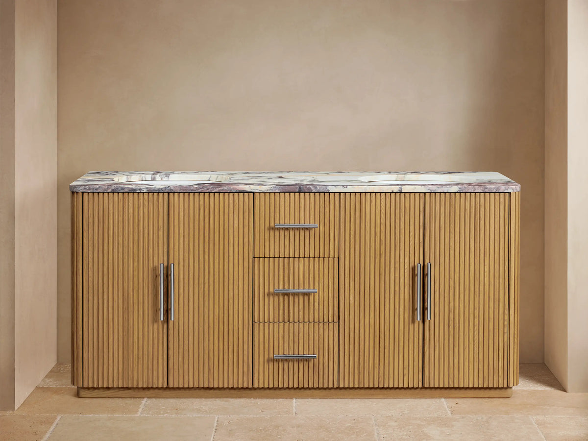 Finnley Double Vanity: ribbed light oak, veined marble top, two sinks, polished nickel hardware. Left door open with towels.