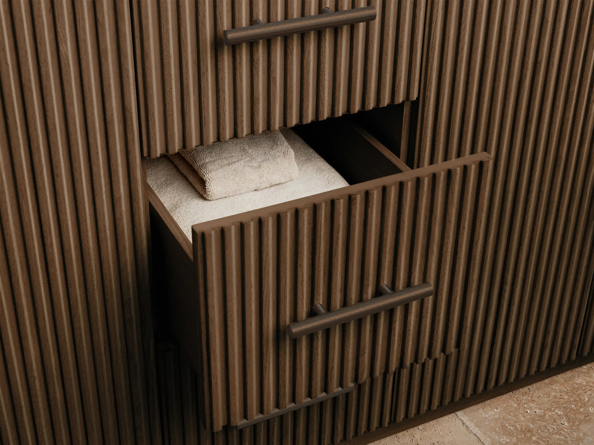 Finnley Double Vanity. Open dark fluted oak cabinet with bronze handle revealing a sponge in a white bowl and stacked white towels.