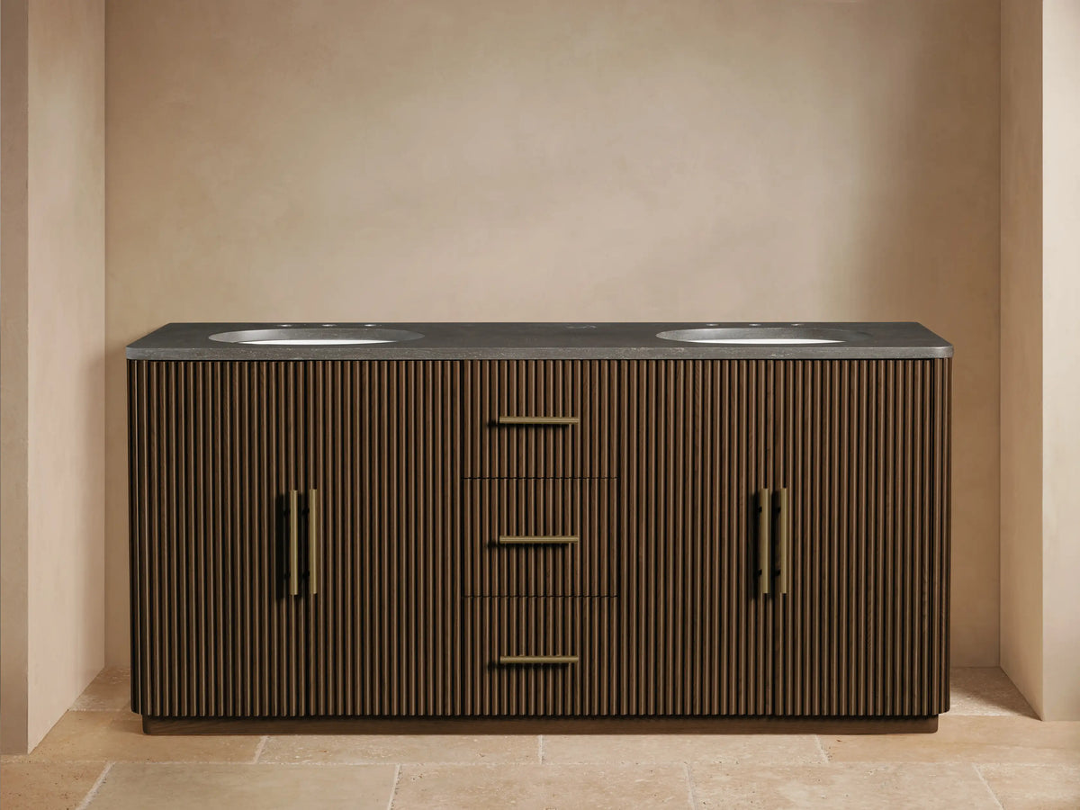 Finnley Double Vanity: dark wood with vertical slats, dark stone top, two white sinks, brass faucets & hardware. Left door open.