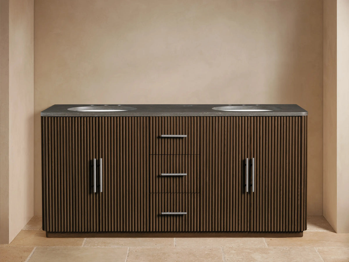 Finnley Double Vanity: dark wood slatted base, dark grey counter, two white sinks, silver faucets, left cabinet open with towels.