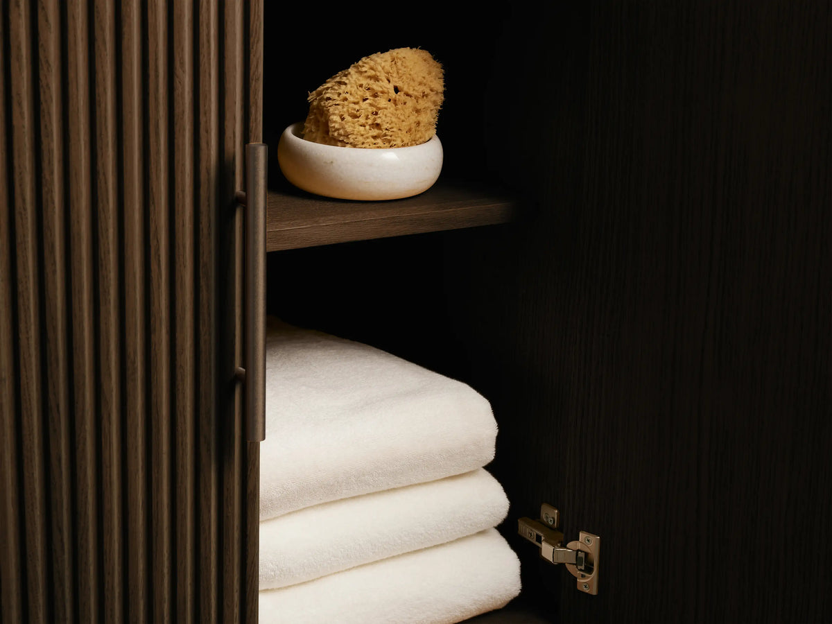 Angled close-up of dark fluted Finnley Double Vanity. A drawer is open, revealing neatly folded beige towels. Bronze hardware.