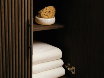 Angled close-up of dark fluted Finnley Double Vanity. A drawer is open, revealing neatly folded beige towels. Bronze hardware.