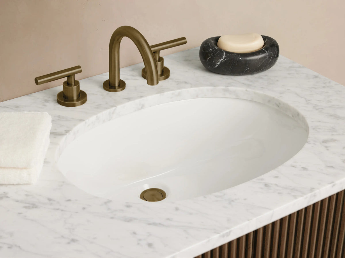 Finnley Double Vanity: Dark fluted wood cabinet, white marble top, two oval sinks, and antique brass hardware against a beige wall.