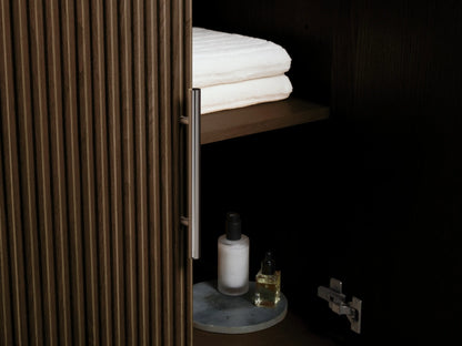 Finnley Double Vanity close-up. Ribbed dark oak drawer slightly open with white towels & bottle. White marble top, silver handle.