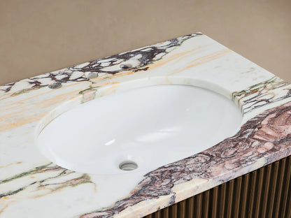 Close-up of Finnley Double Vanity's oval white sink, brass faucet, colorful veined marble countertop, and fluted brown cabinet.