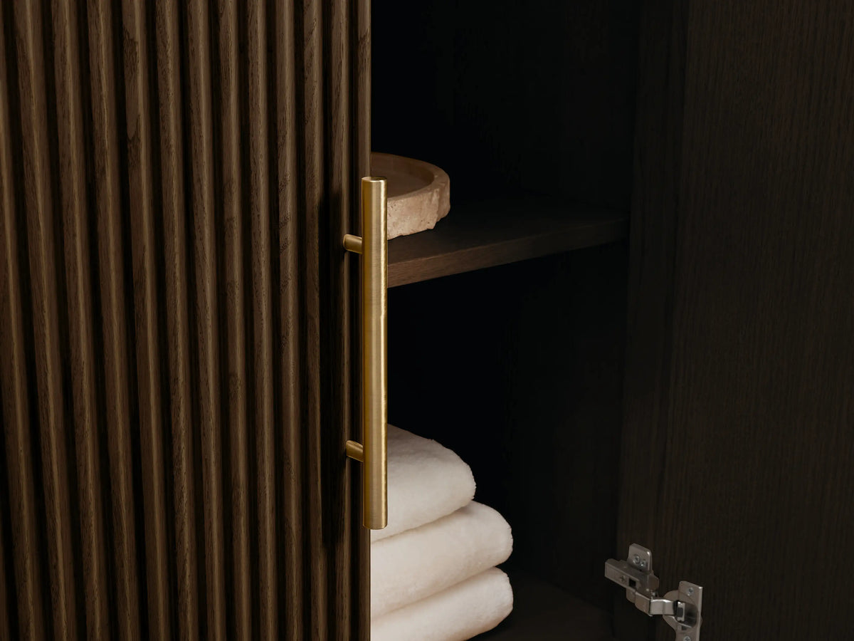 Finnley Double Vanity: close-up of dark fluted wood cabinet, veined red marble top, brass pulls. Drawer open with white towels, bottles.
