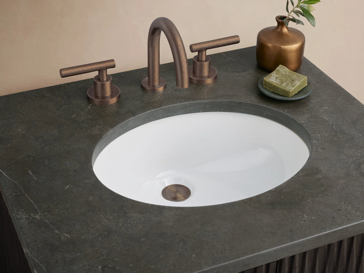 Finnley Powder Vanity: dark fluted wood cabinet, dark stone top with oval sink, and bronze pulls, against a light wall & tiled floor.