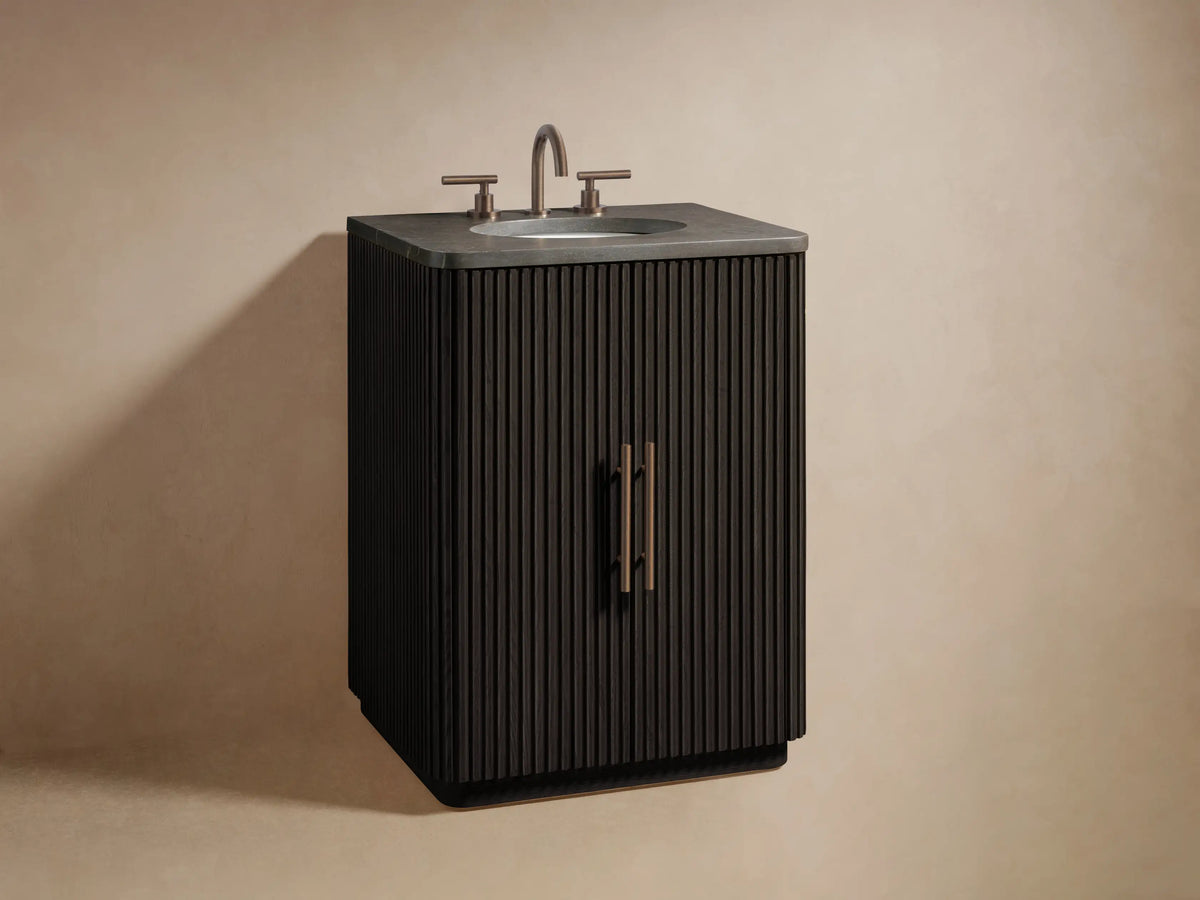 Dark brown Finnley Powder Vanity door with vertical fluting, ajar with brass handle, revealing two bottles and stacked towels.