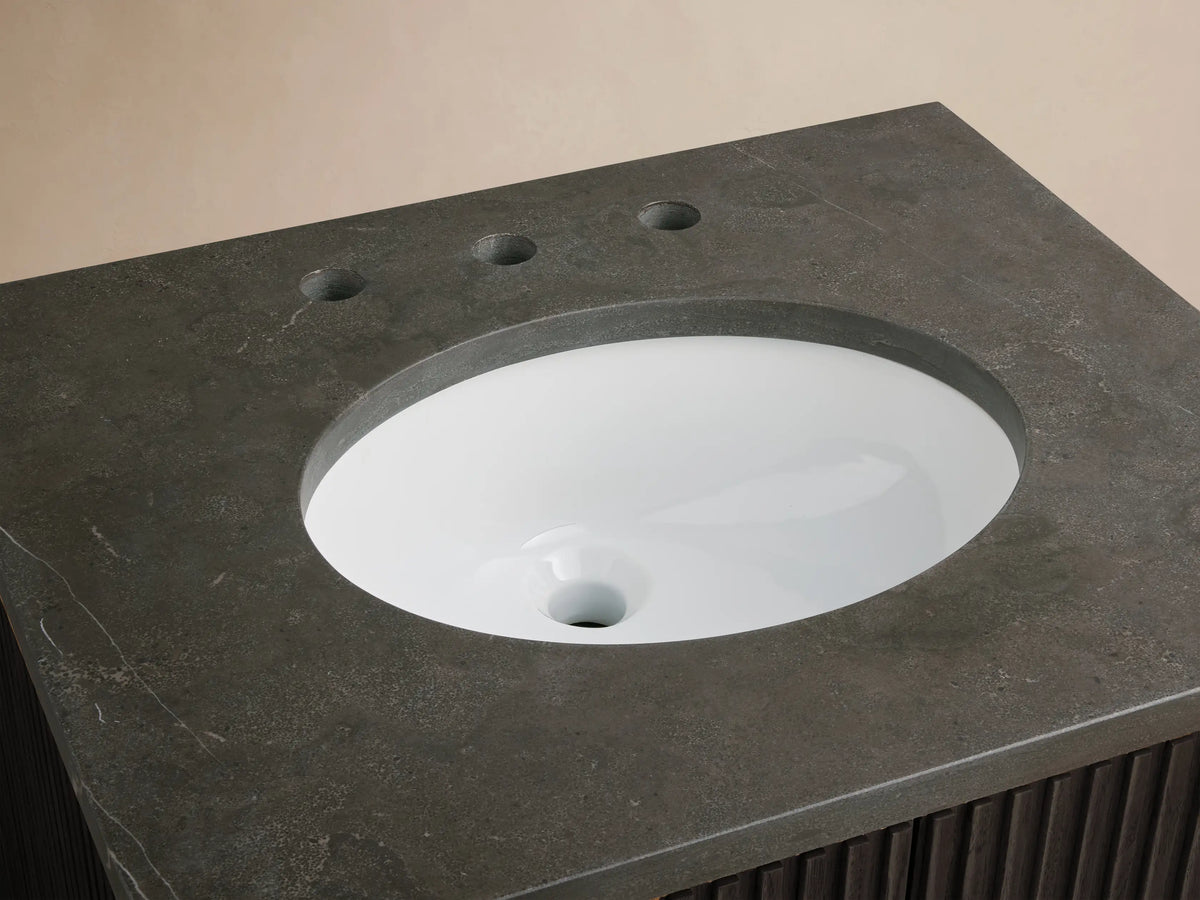 Finnley Powder Vanity with dark stone top, featuring an oval white ceramic sink and pre-drilled holes for a faucet on a neutral background.