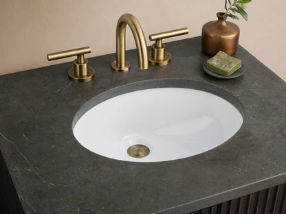 Finnley Powder Vanity with a dark stone countertop, oval white ceramic sink, and antique brass faucet set. Brown decor and green soap highlighted.
