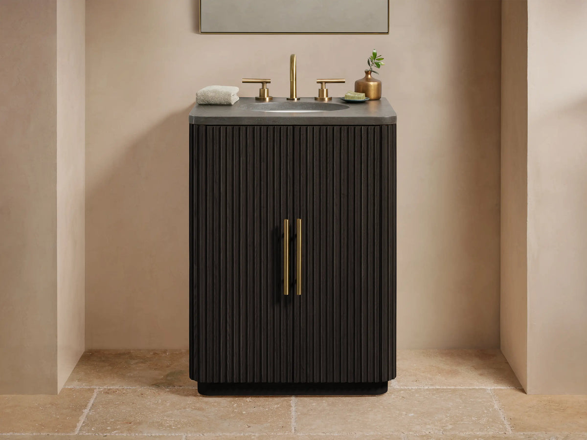 Finnley Powder Vanity in dark wood with ribbed texture, features brass hardware, stone top, and mounted sink on beige tiled floor.