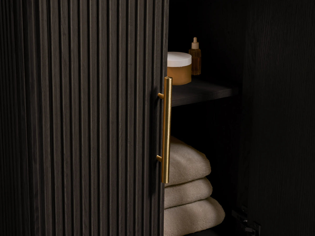 Finnley Powder Vanity in dark wood finish featuring vertical grooves, with a dark stone top, oval ceramic sink, and brass hardware.