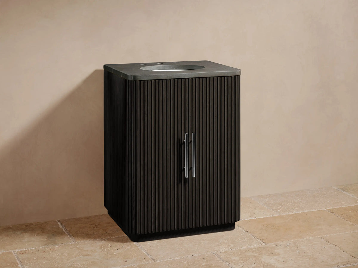 Finnley Powder Vanity with dark vertical slatted wood, oval sink with chrome faucet, on beige tiled floor against a light wall.