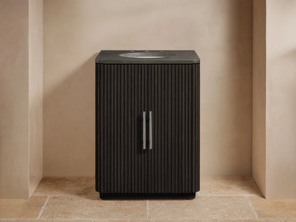 Dark oak wood vanity cabinet door partially open, revealing shelves with neatly folded towels and bottles. Silver vertical handle on ribbed texture.