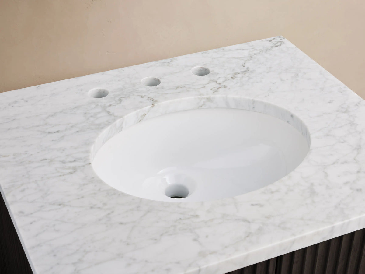 Finnley Powder Vanity: White veined Carrara marble top, oval ceramic sink, bronze faucet, soap, perfume, dark wood base.