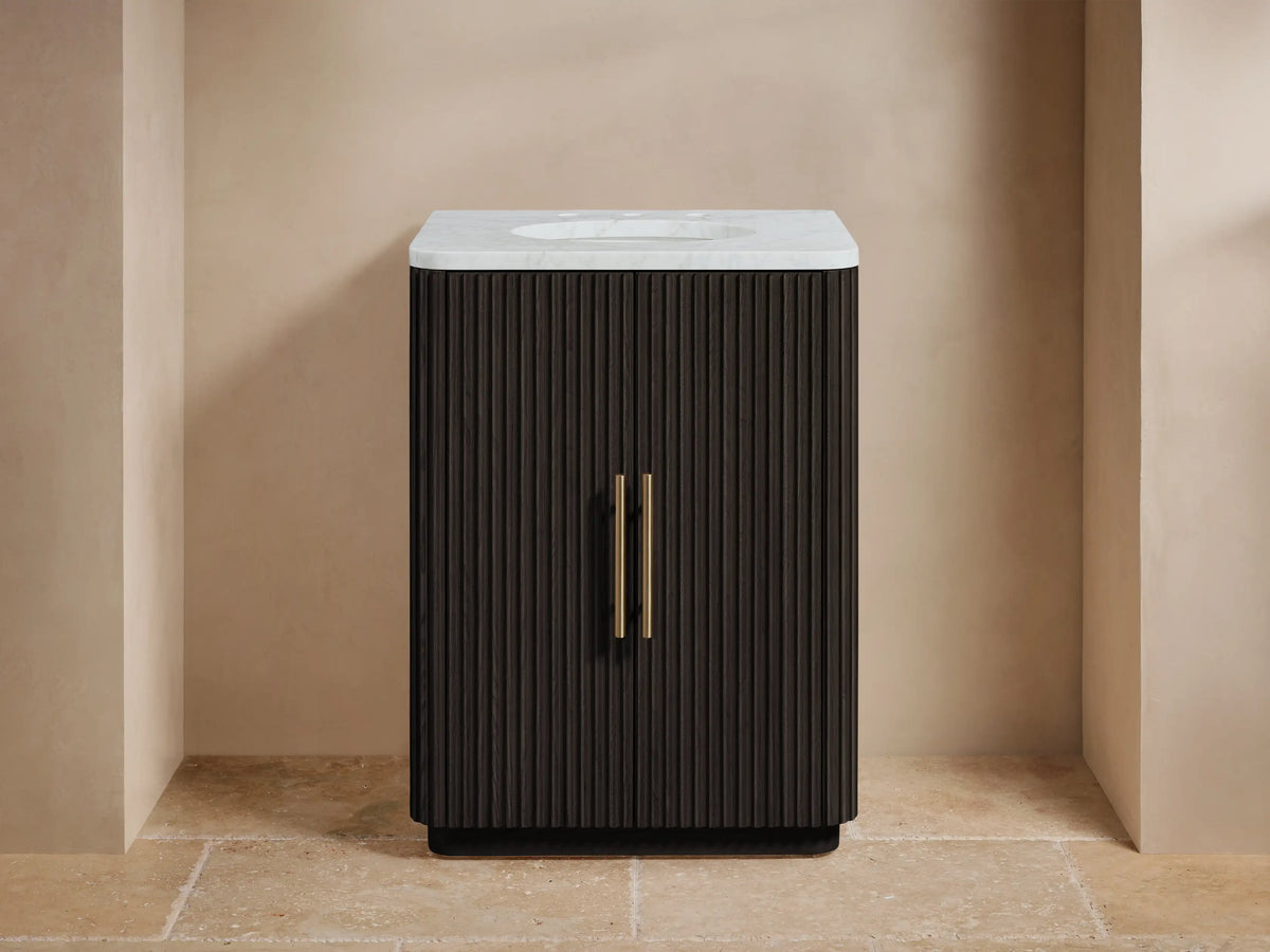 Finnley Powder Vanity with vertical ribbed wood design, white stone top, oval undermount sink, and brass hardware on a beige tile floor.