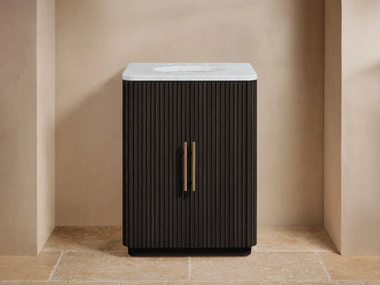 Finnley Powder Vanity with vertical ribbed wood design, white stone top, oval undermount sink, and brass hardware on a beige tile floor.