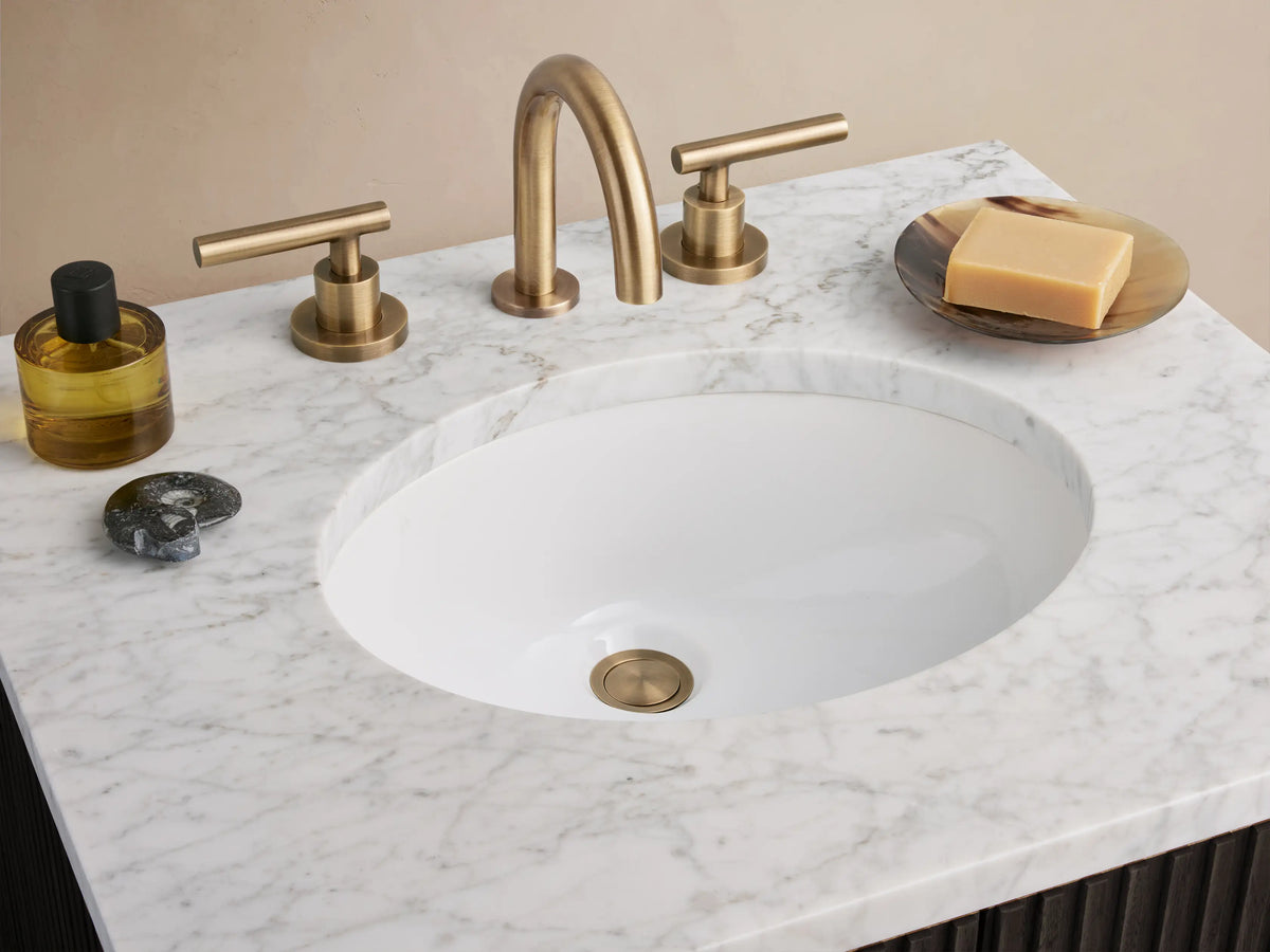 Finnley Powder Vanity with a dark oak wood finish, vertical paneling, white stone top, and antique brass hardware, in a minimal setting.