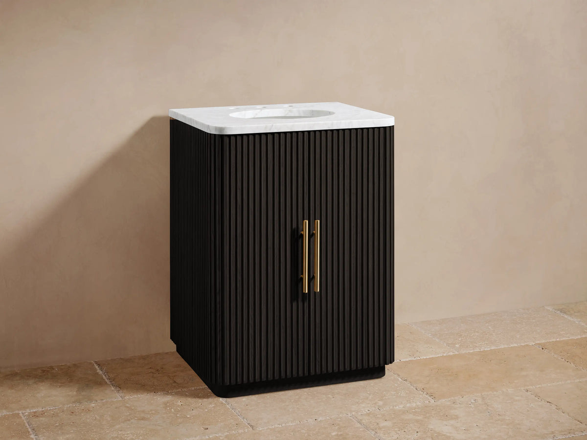 Finnley Powder Vanity in dark oak with vertical grooves, white stone top, oval sink, and antique brass hardware on beige tile floor.