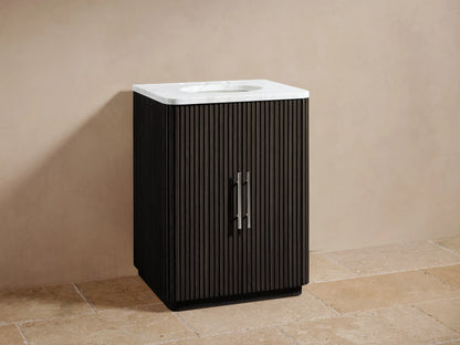 Finnley Powder Vanity with ribbed oak wood finish, white stone top, oval ceramic sink, chrome faucet against beige wall and tiled floor.