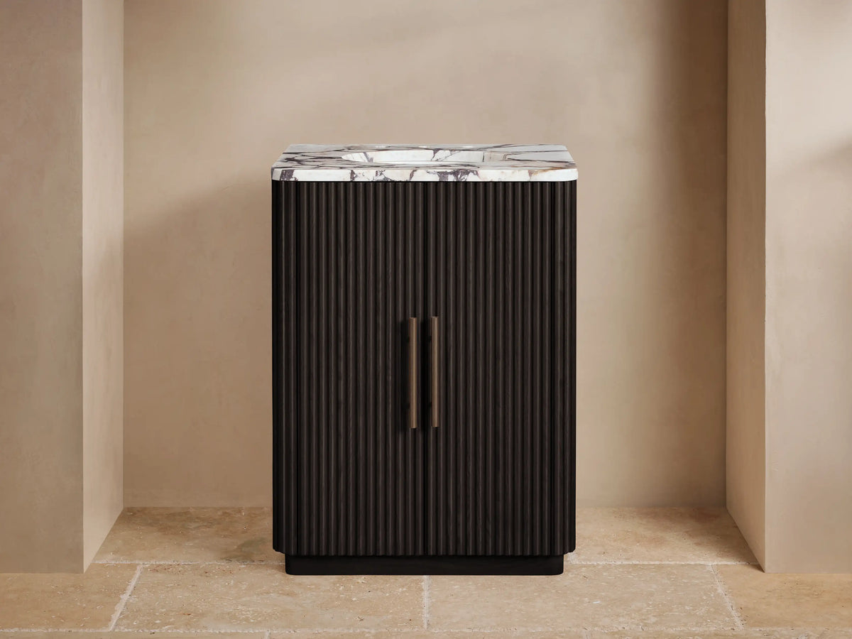 Finnley Powder Vanity: dark reeded wood cabinet with white veined marble top, bronze faucet, soap dispenser, and small plant.