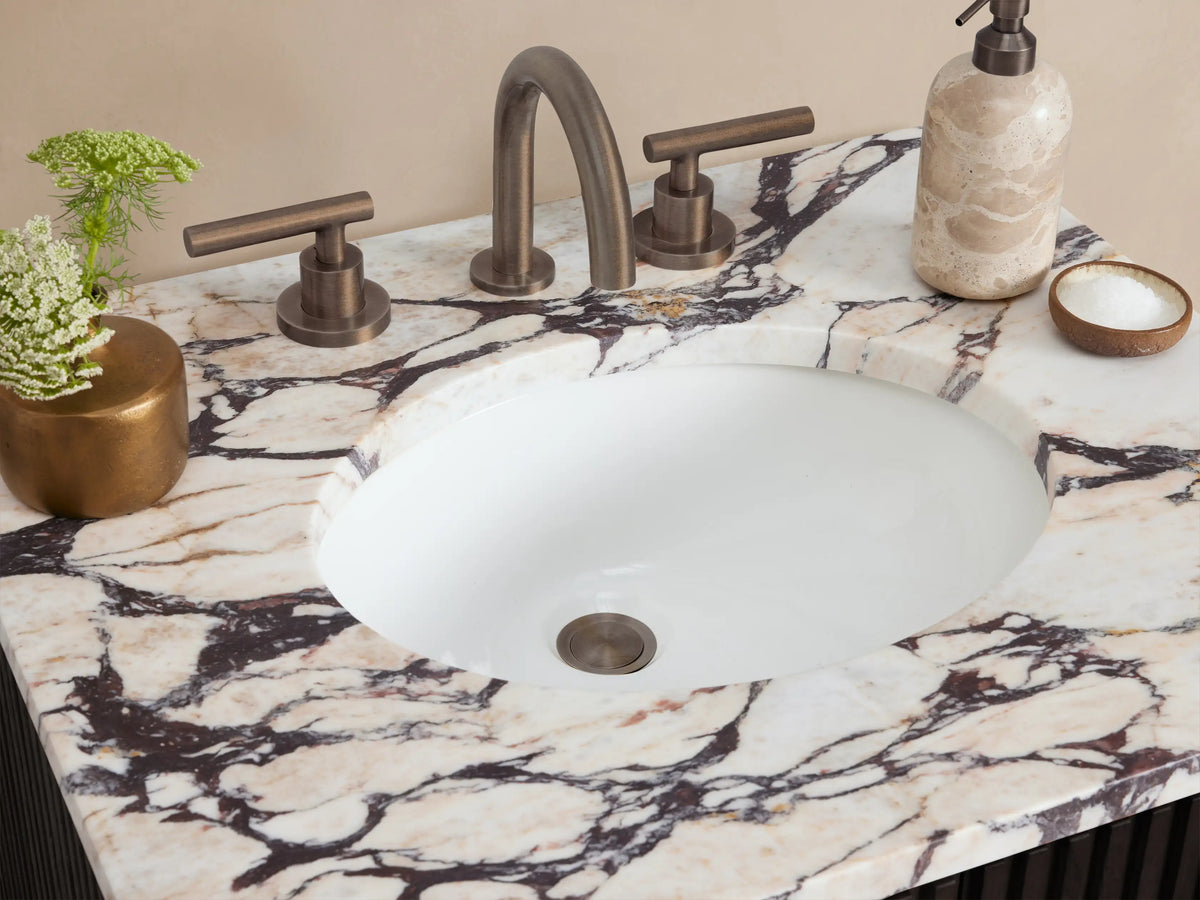 Finnley Powder Vanity: dark fluted wood cabinet with ornate white marble top & bronze handles, centered, front view on stone floor.