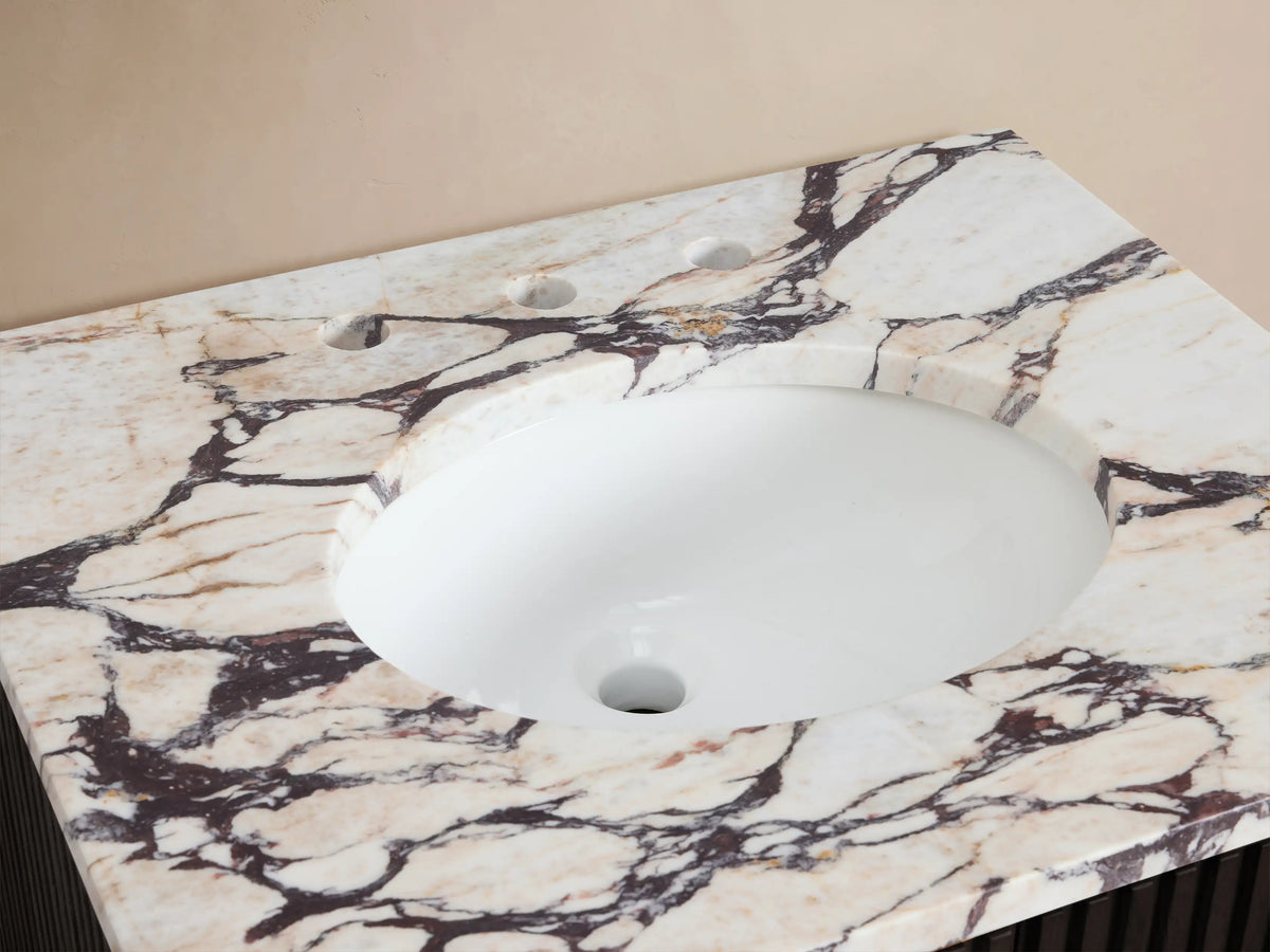 Finnley Powder Vanity countertop: white marble with dark veining, oval white ceramic sink, bronze widespread faucet, accessories.