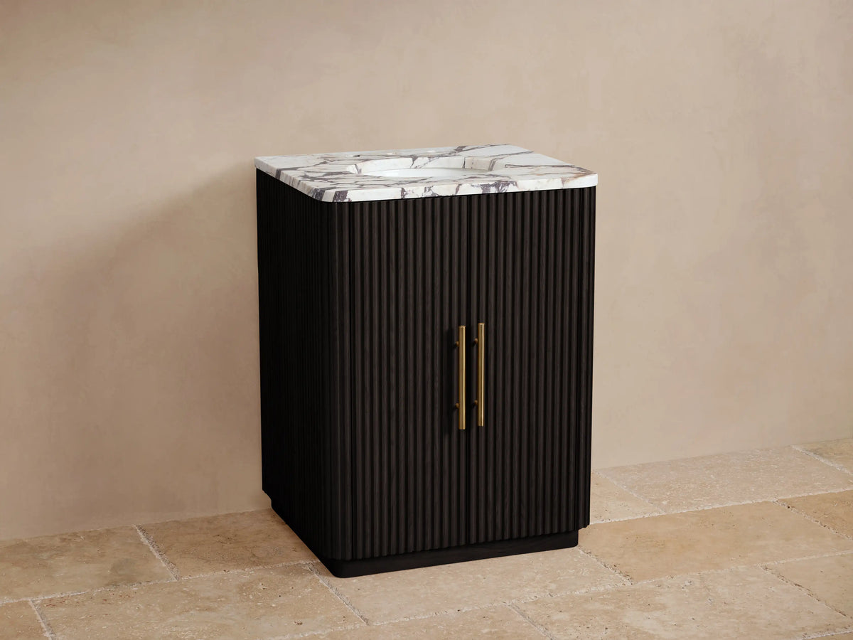Finnley Powder Vanity: Black fluted cabinet, white Carrara marble top, oval sink, gold faucet & handles, on tiled floor.