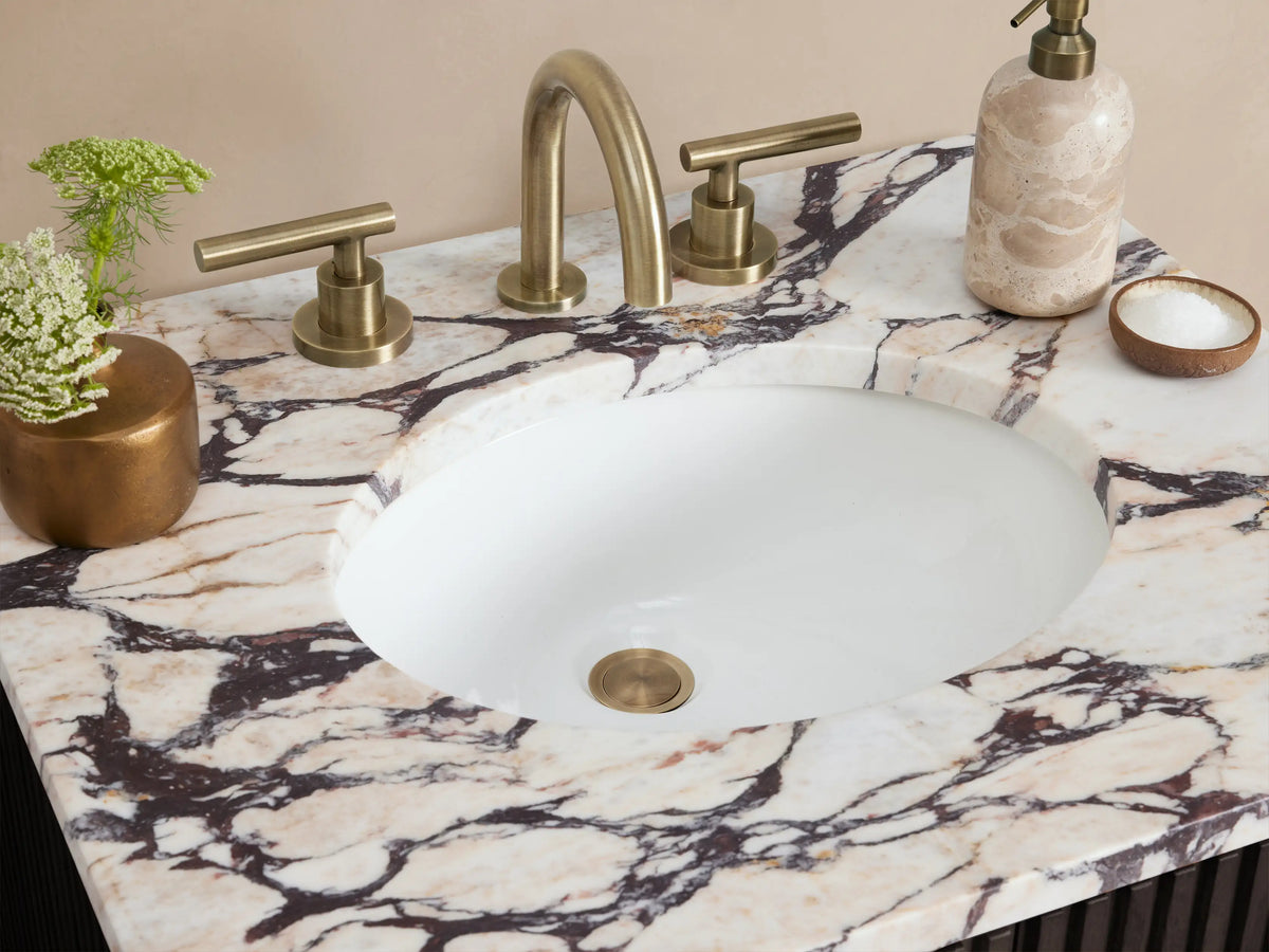 Finnley Powder Vanity: black fluted cabinet, white marble top with sink, gold handles, on tiled floor against beige wall.