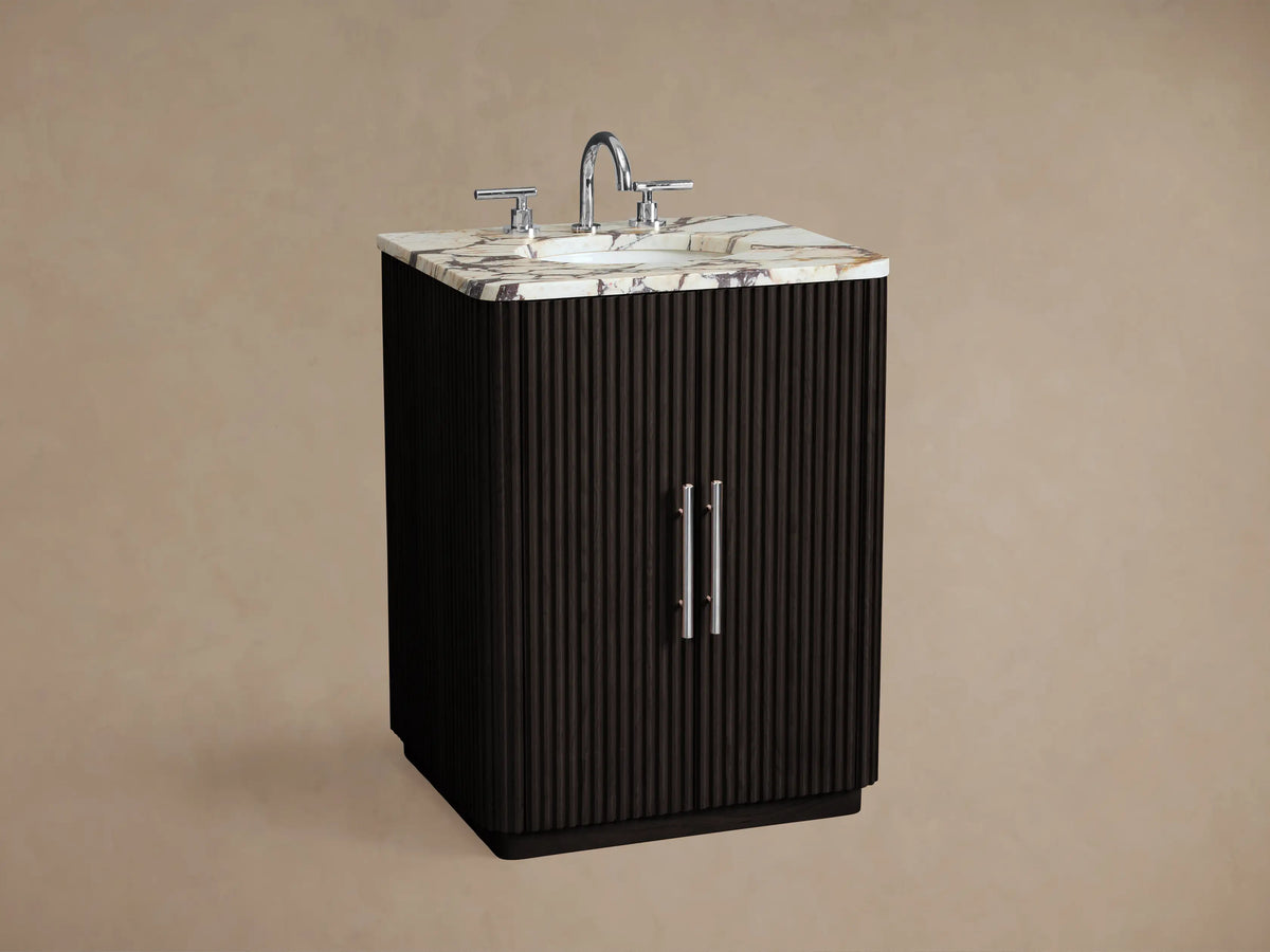 Front view of Finnley Powder Vanity. Dark fluted wood cabinet, veined white marble top, 2 polished nickel pulls. On stone floor.