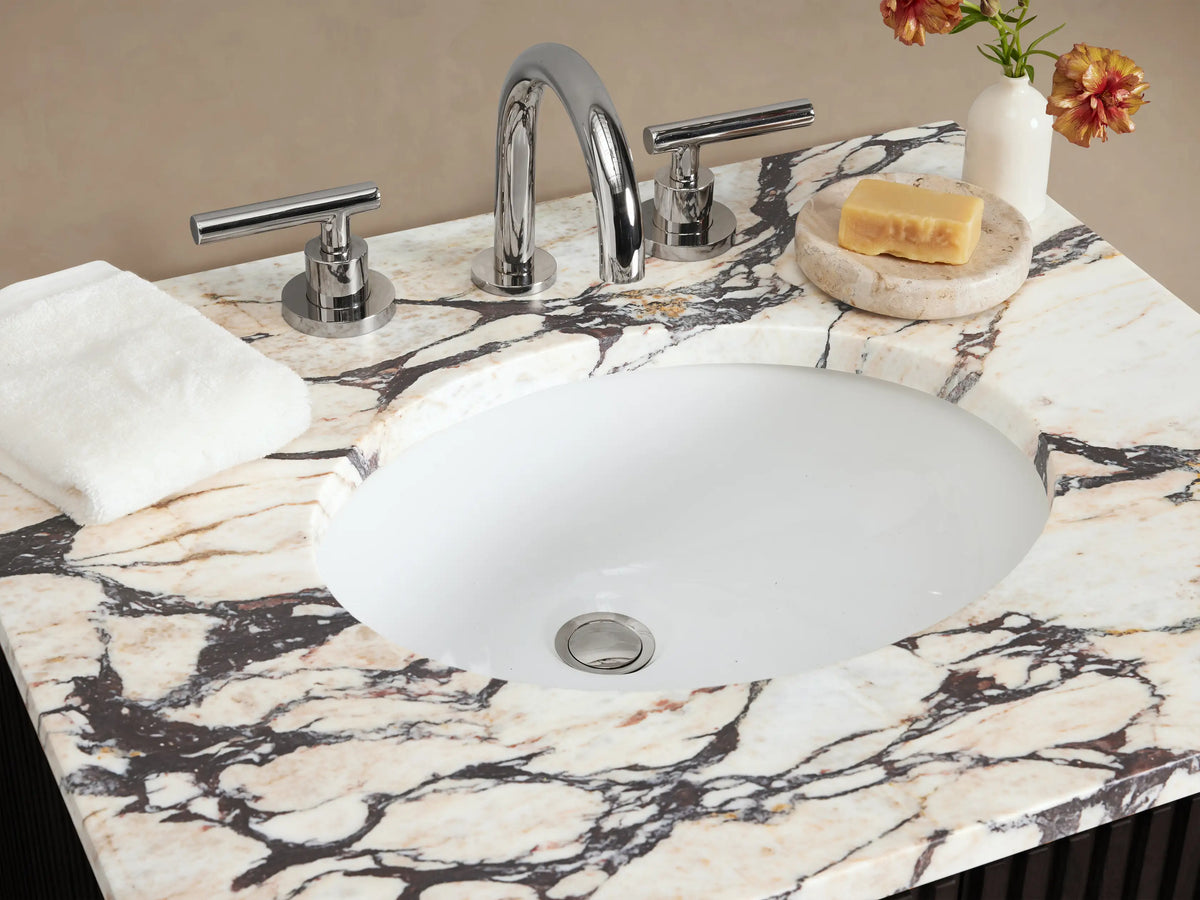 Finnley Powder Vanity: Dark fluted cabinet with white Carrara marble top, oval sink, and polished nickel handles.