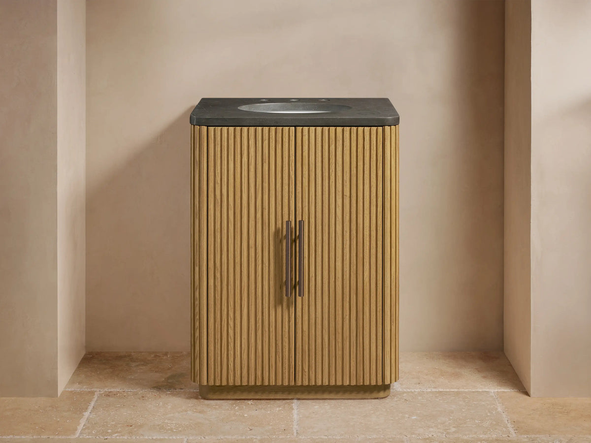 Finnley Powder Vanity with light oak ribbed cabinet, dark grey stone top, bronze faucet, towel, and vase in a neutral room.