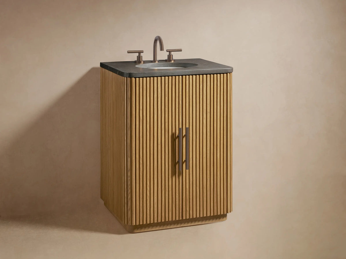 Close-up of Finnley Powder Vanity's open oak cabinet door with fluted texture, dark handle, revealing a shelf with toiletries and stacked gray towels.