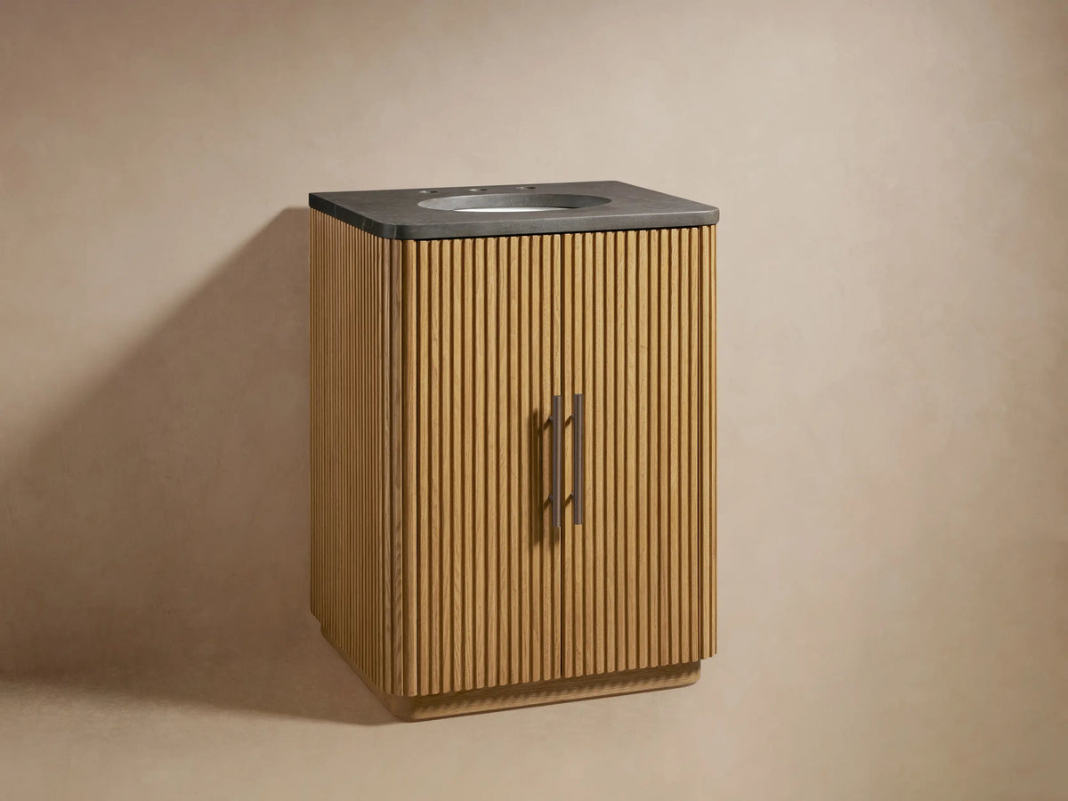 Finnley Powder Vanity with light reeded wood cabinet, dark stone top, integrated sink, and bronze faucet & handles.