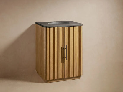Finnley Powder Vanity with light reeded wood cabinet, dark stone top, integrated sink, and bronze faucet & handles.