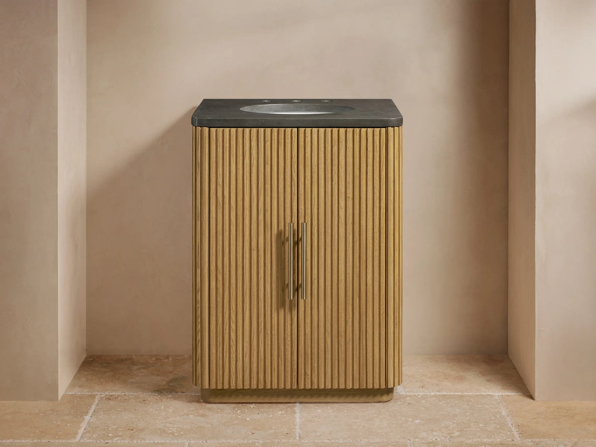 Finnley Powder Vanity with oak wood slatted cabinet, dark stone top, oval sink, and Antique Brass hardware in a neutral-toned bathroom.