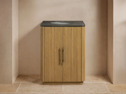 Finnley Powder Vanity with oak wood slatted cabinet, dark stone top, oval sink, and Antique Brass hardware in a neutral-toned bathroom.