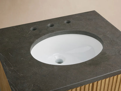 Finnley Powder Vanity featuring a dark stone top with an oval ceramic sink, antique brass fixtures, soap, and a vase on the side.