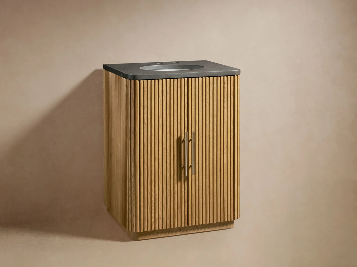 Finnley Powder Vanity showing partially open oak wood door with vertical grooves, revealing towels and bottles on shelves, with brass handle.