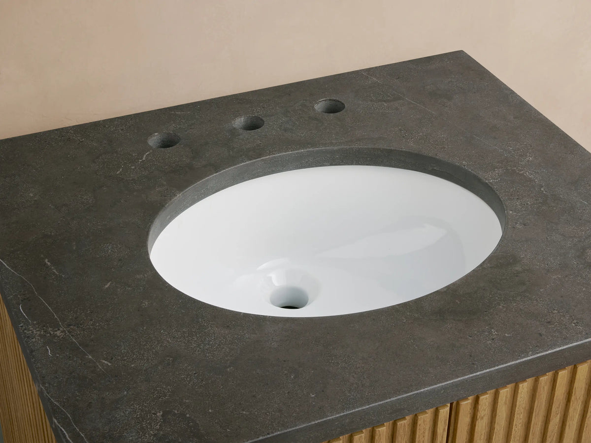 Oval undermount sink set in a honed stone countertop with bluestone finish, featuring polished nickel faucet fixtures.