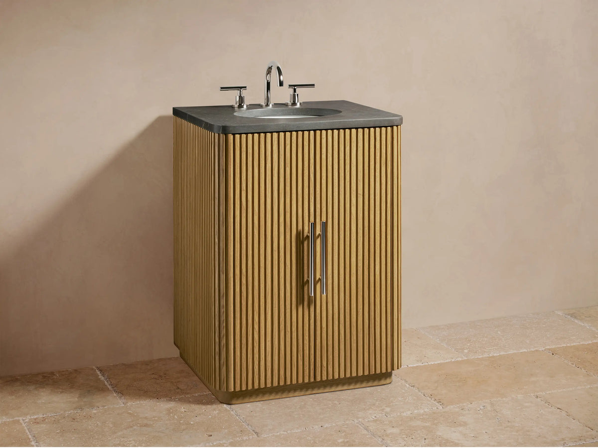 Open door of the Finnley Powder Vanity showing oak wood with vertical grooves, shelves with folded towels, and a small bottle.