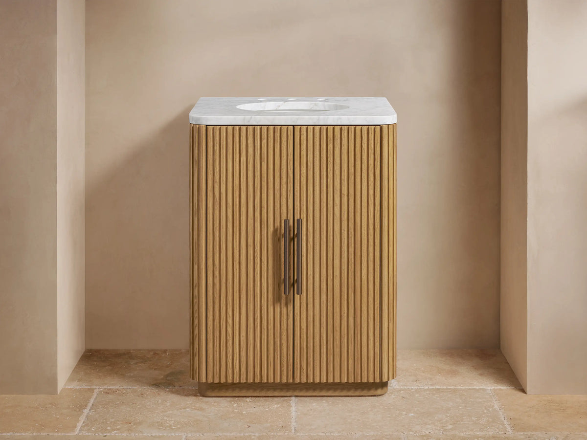 Finnley Powder Vanity: Fluted light oak wood cabinet with white Carrara marble top, antique bronze faucet, and handles.