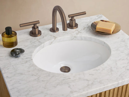 Finnley Powder Vanity: light oak cabinet, vertical fluting, dark handles, white marble top, oval sink, against a beige wall.