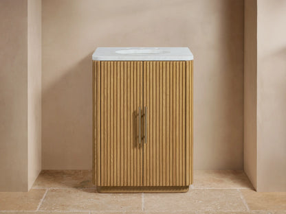 Oak wood vanity with vertical slat design, stone top, oval ceramic sink, and two brass-finished handles; beige backdrop.