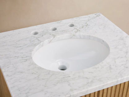 Oval ceramic undermount sink with Carrara marble countertop and antique brass faucet, flanked by soap and accessory on the Finnley Powder Vanity.