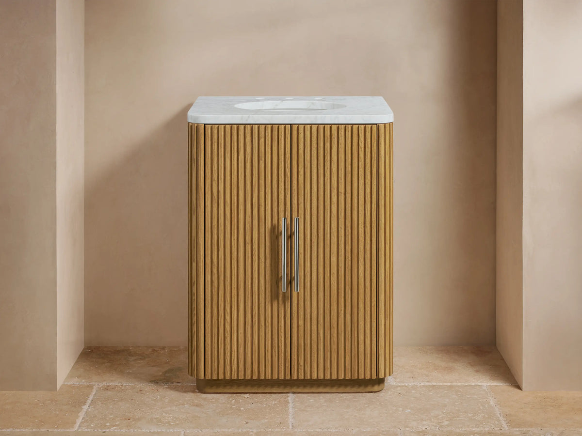 Finnley Powder Vanity with oak wood slatted front, white stone top, and oval sink; faucet with dual handles, greenery in vase.