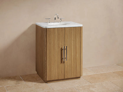 Open oak cabinet with vertical grooves, showing shelves containing folded beige towels and a small jar, metal handle on door.