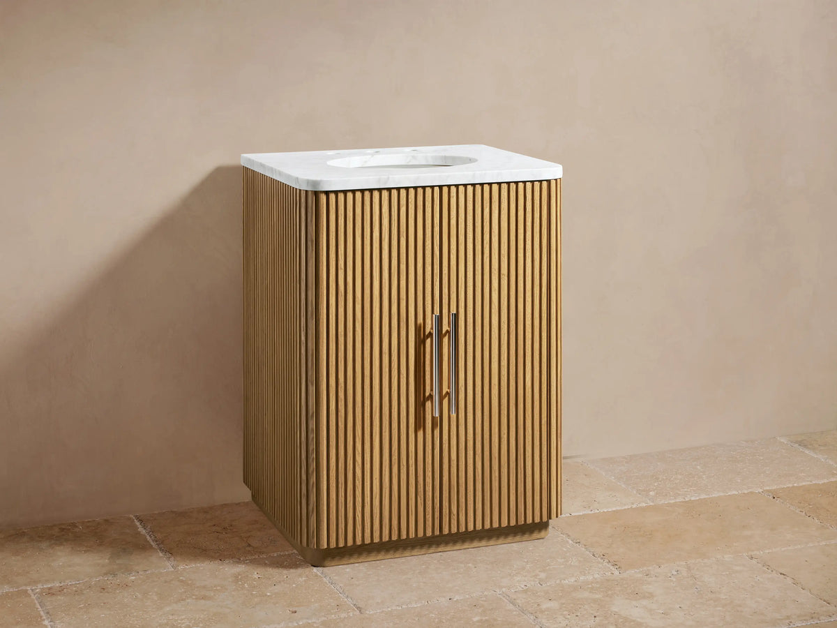 Finnley Powder Vanity with slatted oak wood finish, Carrara marble top, dual faucets, and oval sink, against a beige wall.