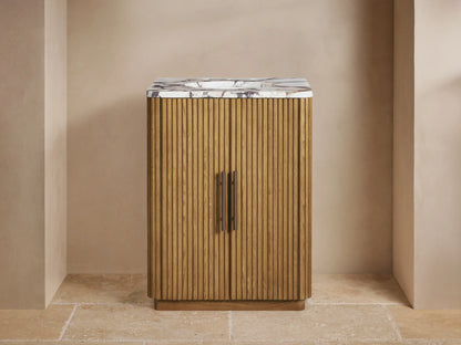 Finnley Powder Vanity: Ribbed oak cabinet, white marble top with bronze faucet & handles, against a beige wall on stone floor.