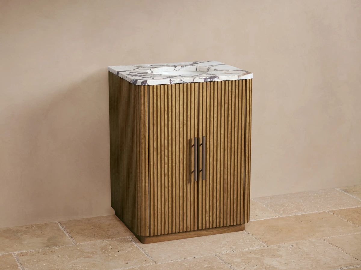 Finnley Powder Vanity: Warm oak wood with fluted doors, white marble top with grey veining, oval sink, and dark bronze faucet.
